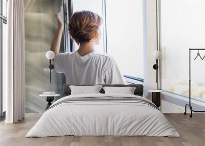 Young woman opening window in living room for fresh air Wall mural